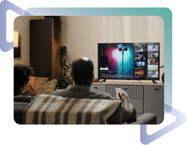 A person sitting on a couch with a child, watching a TV displaying a movie menu in a cozy living room with plants and soft lighting.