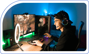 A person wearing headphones and a cap is gaming on a dual-monitor setup. The room is dimly lit with neon blue lighting, creating an immersive atmosphere.